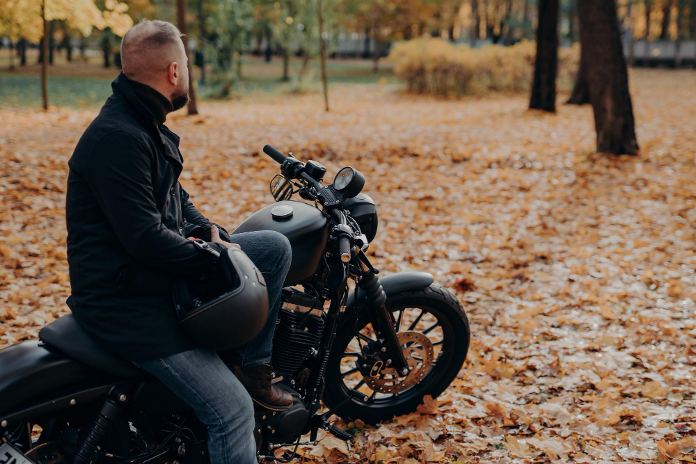 back-view-bearded-male-biker-looks-thoughtfully-somewhere-into-distance-poses-black-motorbike-holds-protective-helmet-spends-leisure-time-autumnal-park-copy-space-your-advertising