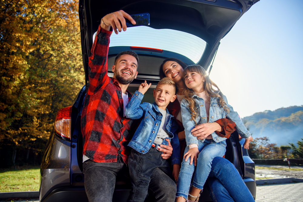 happy-stylish-parents-with-their-cute-lovely-children-are-making-funny-selfie-smart-phone-while-sitting-trunk-happy-modern-family-concept