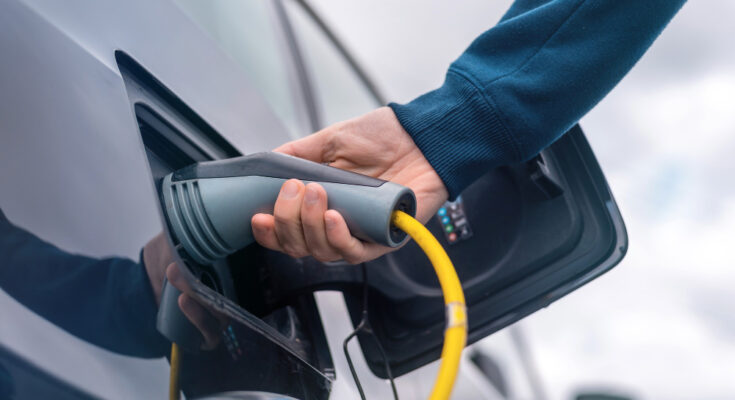Man Plugging Charger Into Electric Car Charge Station